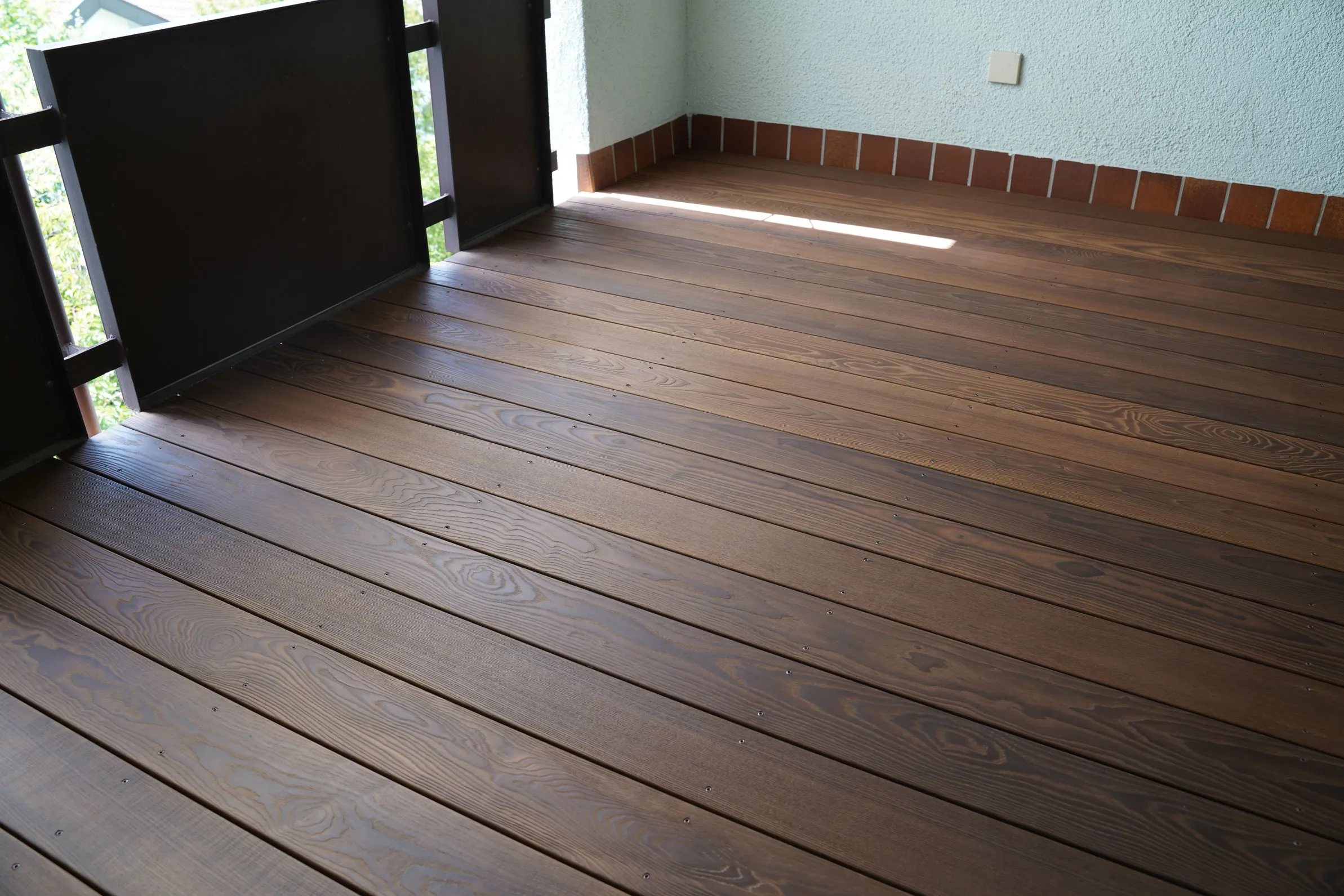 Balkon mit dunkel geölter Holzterrasse und hölzernem Sichtschutz