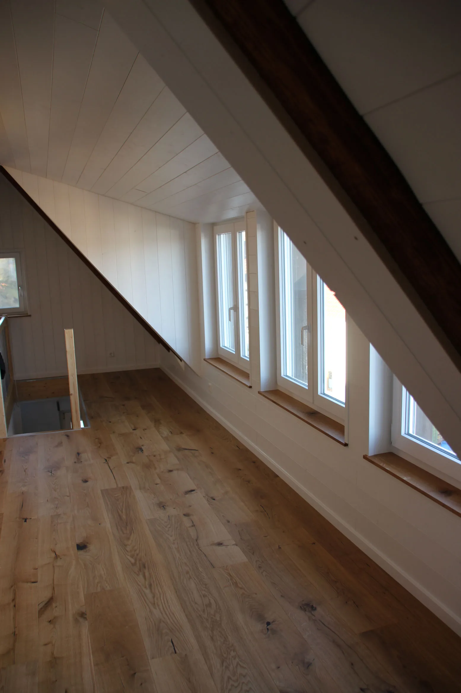 Ausgebauter Dachboden mit weiß lasierter Holzverkleidung, Fensterband und Eichendielen